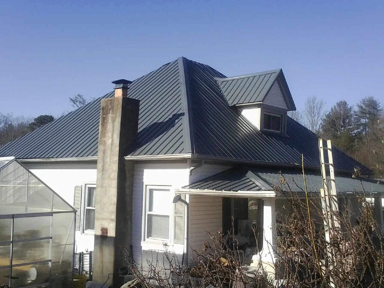 Dark blue standing seam metal roof on a white farmhouse with dormer — Slate & Tile Roof Repair by Roofing Brothers in Valley Spring