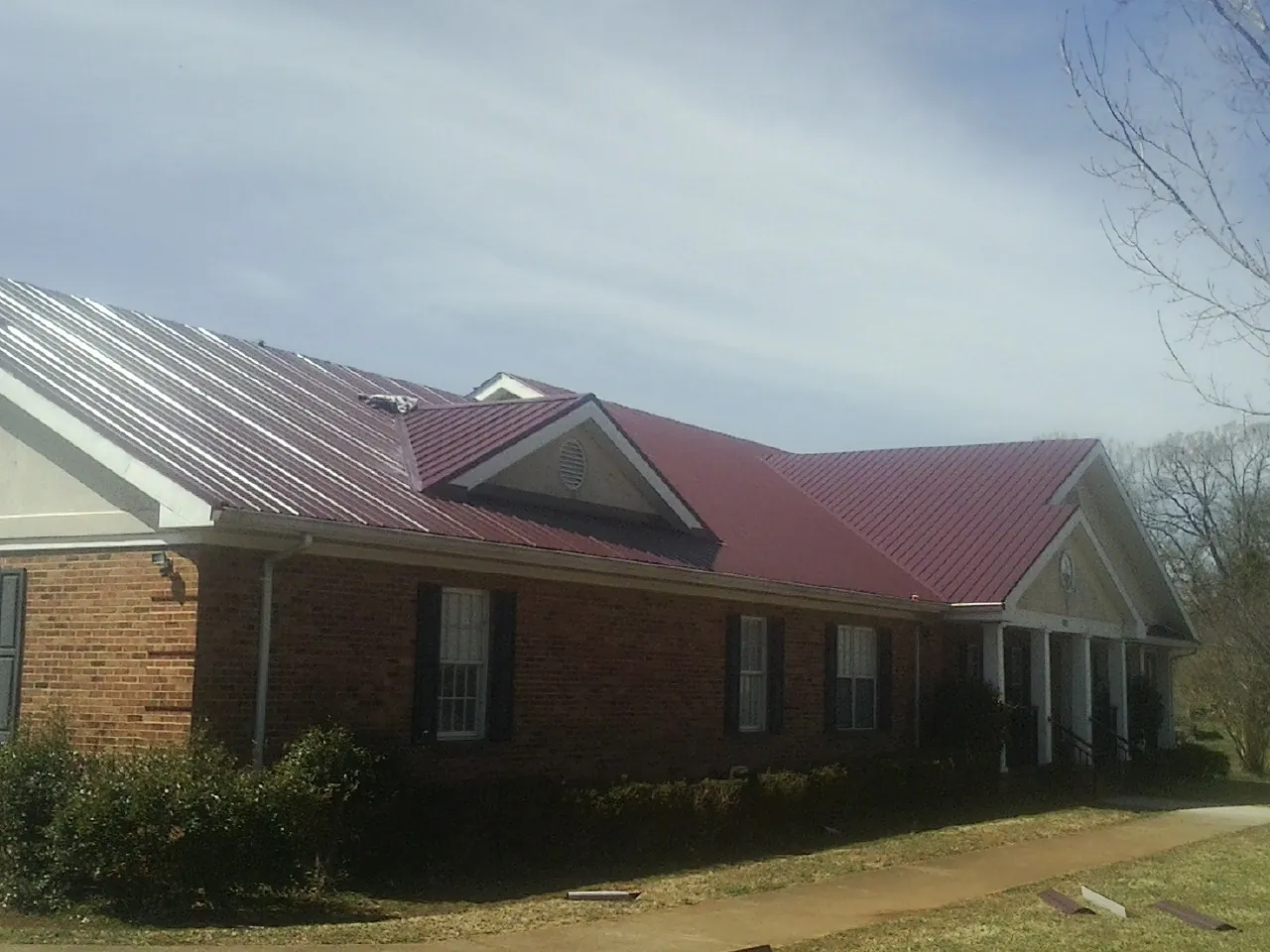 Red metal roof with gabled entries on a long brick building, from a Hail Damage Roof Repair job in Valley Spring