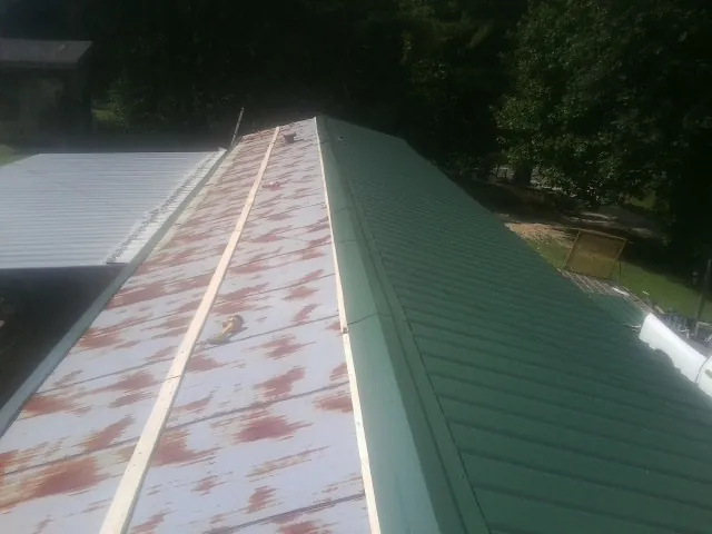 Old rusted panels beside newly installed green metal roofing — Wind Damage Roof Repair by Roofing Brothers in Valley Spring