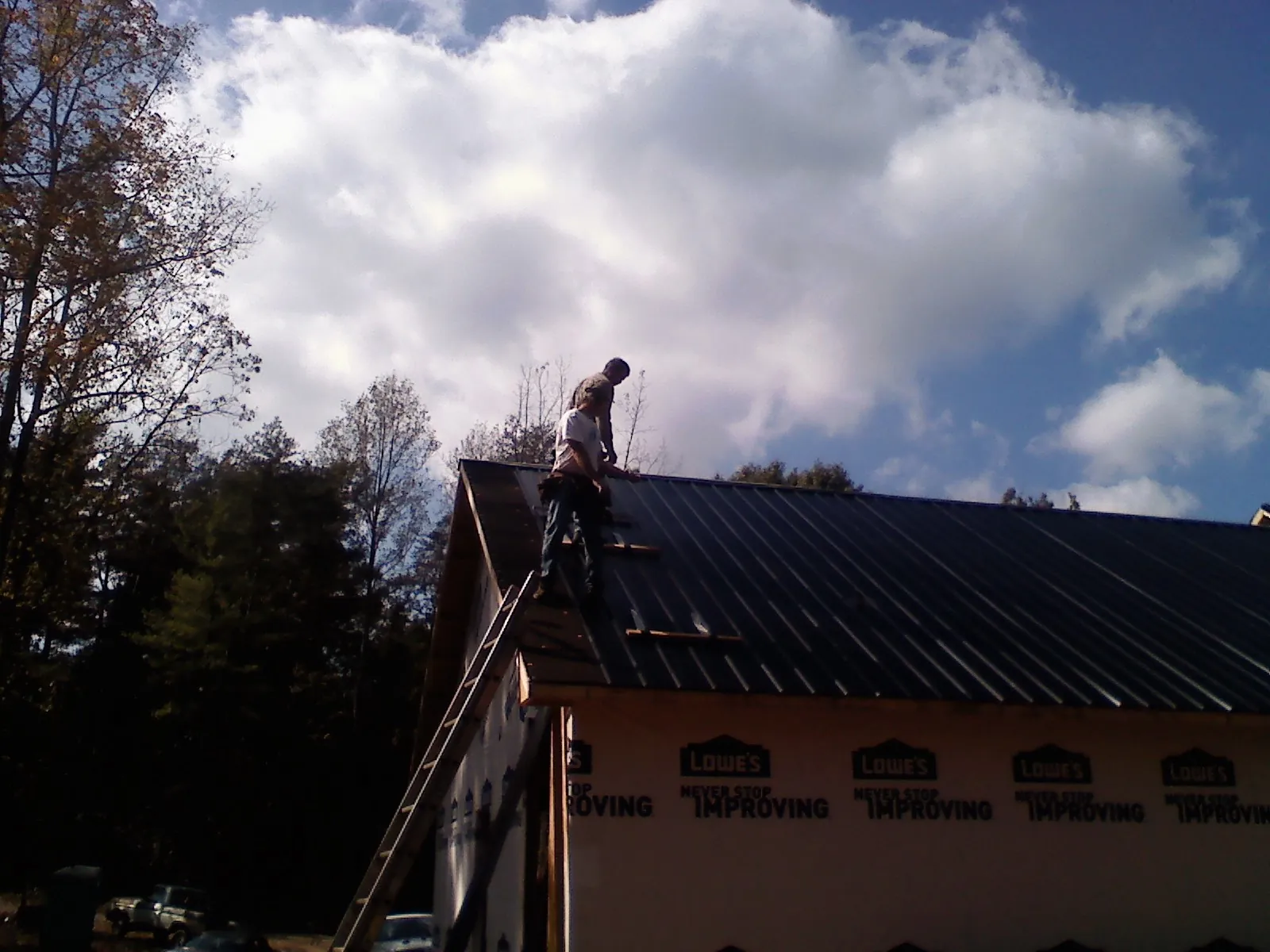 Roofer fastening dark metal panels high against a cloudy sky, from a Roof Inspection job in Valley Spring