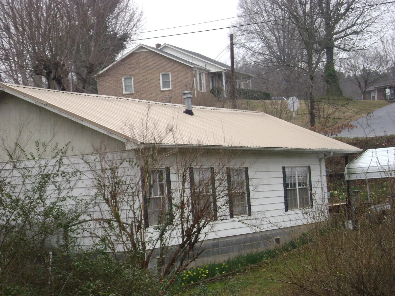Tan metal roof on a white sided house set into a hillside — Commercial Roofing by Roofing Brothers in Valley Spring